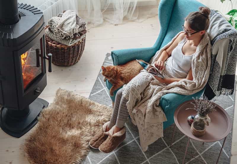 young-woman-by-fireplace-sitting-cozy-armchair-with-warm-blanket-using-tablet1