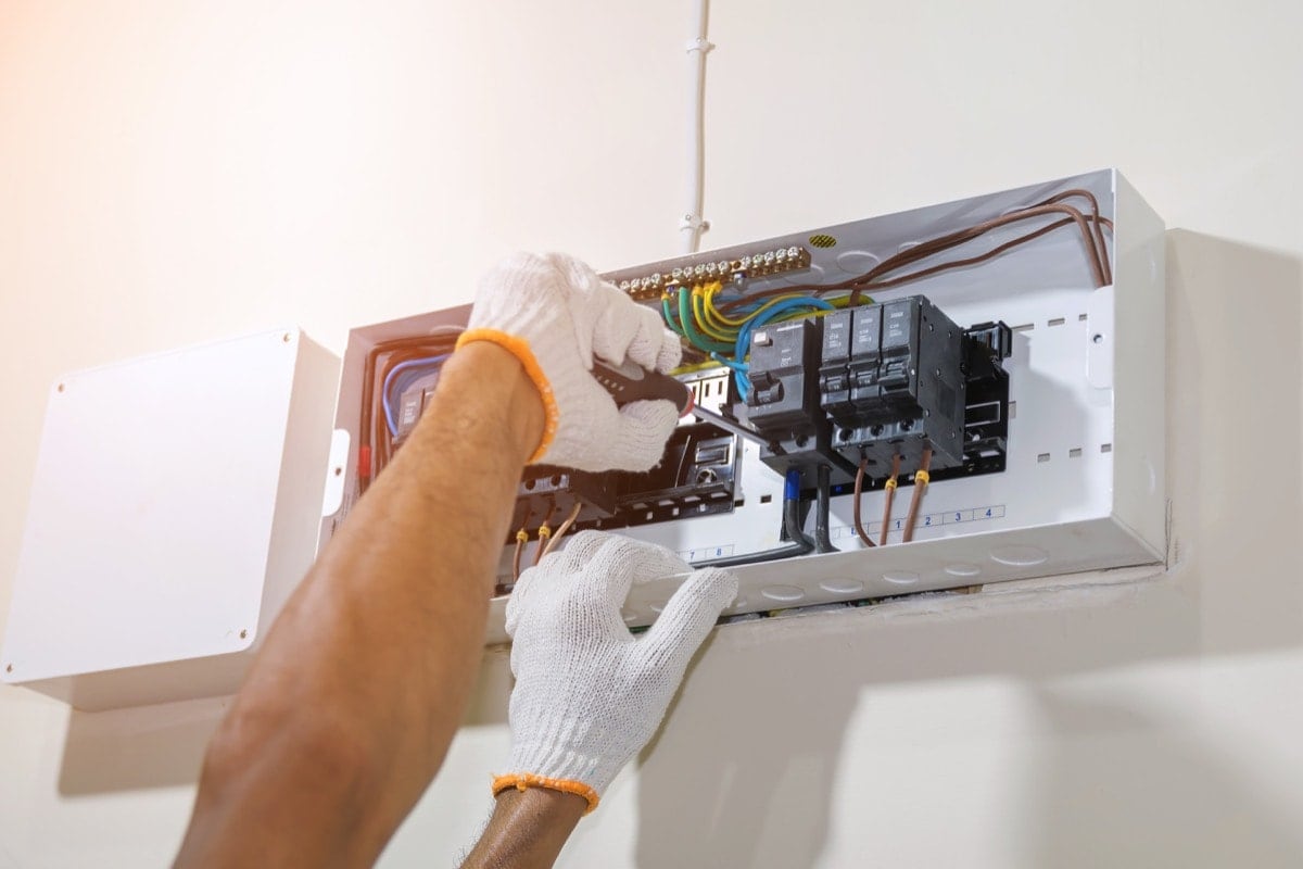 gloved hands of electrician repairing electrical panel