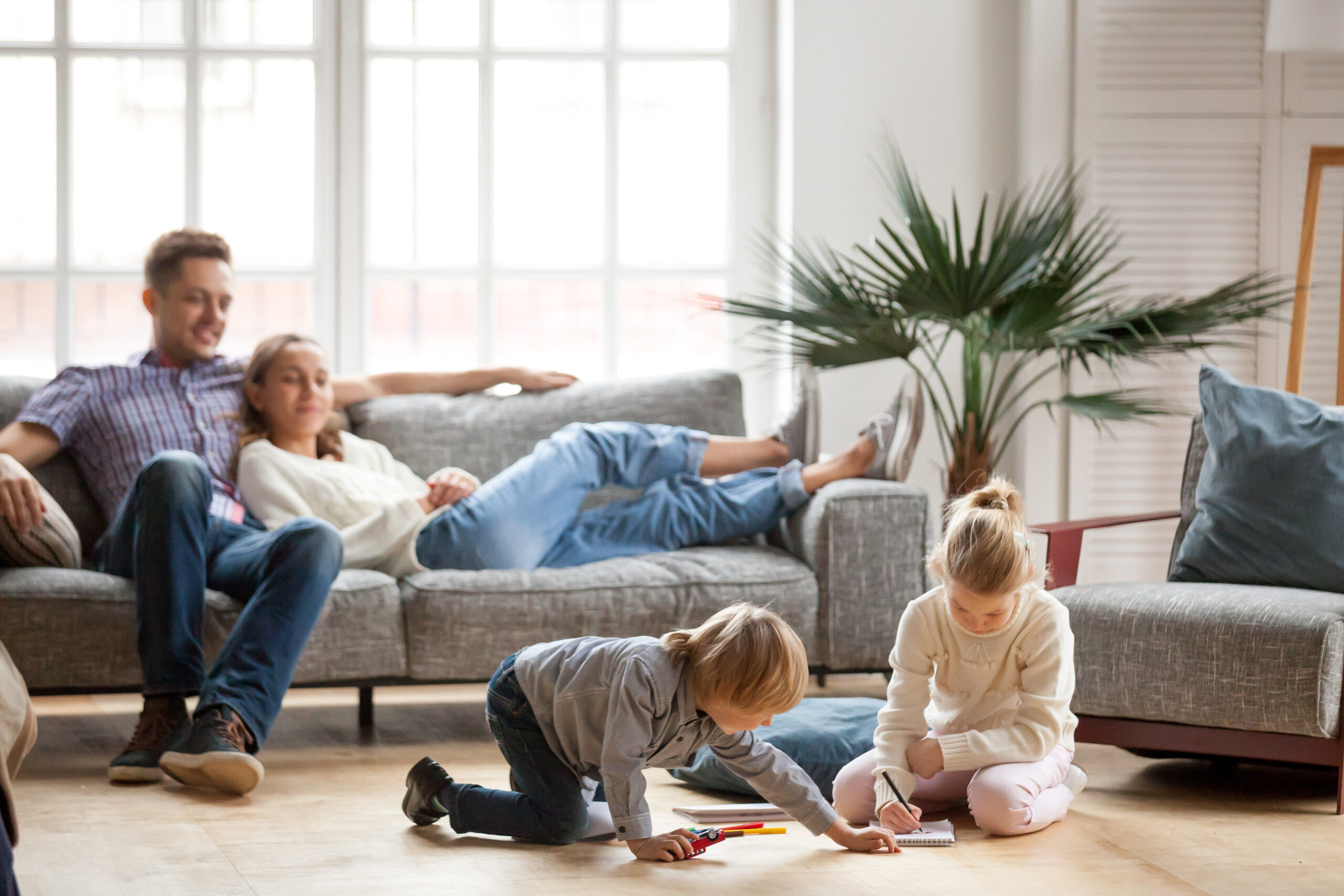 mother and father relaxing on couch watching son and daughter play on floor